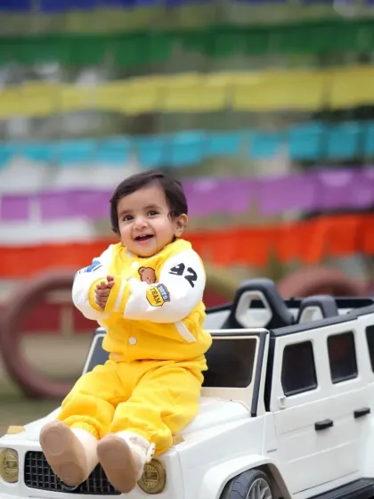 A happy baby enjoying the ride, sitting on the hood of his toy car during a fun and colorful outdoor photoshoot.