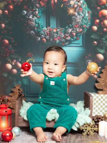 A vibrant and festive Christmas setup. This little one is ready for Santa with his green overalls and a backdrop full of holiday cheer.