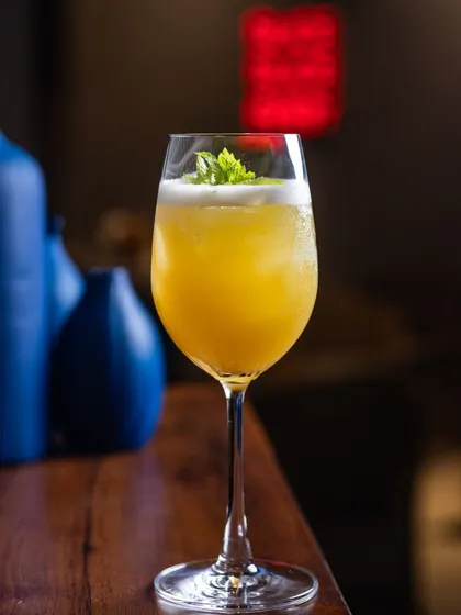 A bright, citrus-colored mocktail served in a wine glass with a mint garnish. My handcrafted drinks are designed to elevate your refreshment game with sophisticated flavors.