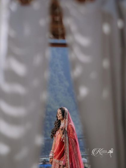 A creative shot of a bride framed by white curtains, with mountains visible in the background.