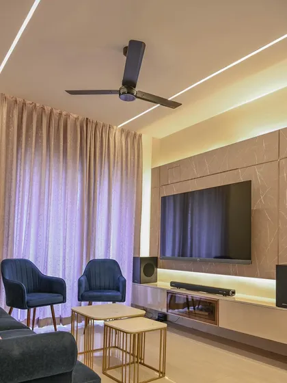 In the Aarohi Residence, we designed a contemporary living room with a focus on clean lines and sophisticated lighting. The marble-finish wall panel behind the TV is complemented by recessed cove lighting and linear ceiling lights, creating a sleek and modern media zone.