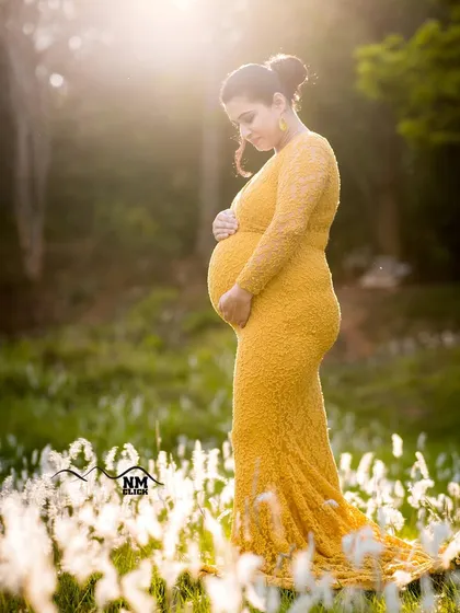 A quiet, reflective moment during an outdoor maternity shoot. The soft, golden light filtering through the trees highlights the beautiful silhouette of the baby bump, creating a portrait filled with peace and anticipation.
