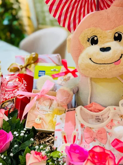 A close-up view of the handpicked items, including soft baby clothes and essentials, nestled amongst fresh pink roses.