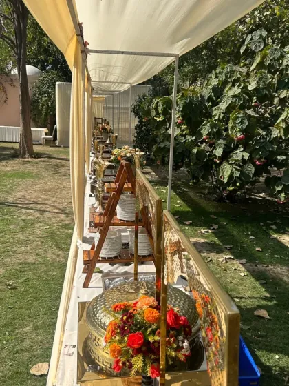 A detailed view of our buffet arrangement for a sunny outdoor event. The combination of golden serving dishes and fresh floral bouquets creates a bright and welcoming food station for guests.