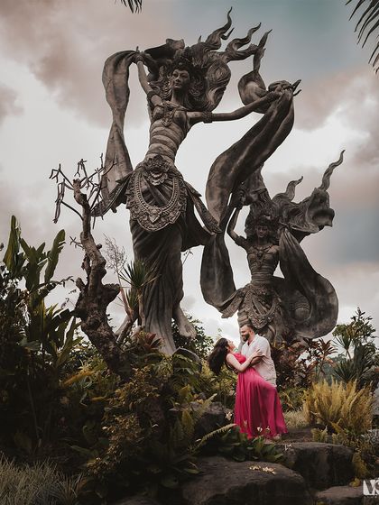 A romantic portrait of a couple embracing at the foot of a towering statue in Bali. The dramatic sky and grand scale make this an epic and memorable pre-wedding image.