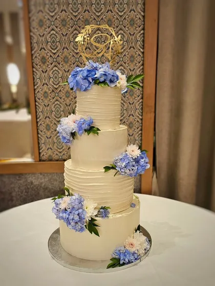 The final four-tier wedding cake, elegantly decorated with fresh blue and white hydrangeas and a custom gold monogram topper.