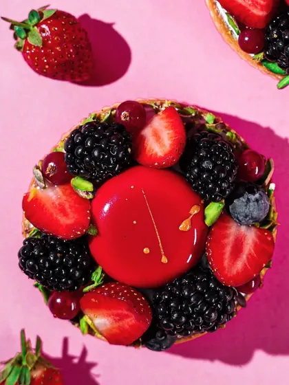 A top-down shot of a stunning berry tart, with a glossy red center surrounded by fresh strawberries, blackberries, and blueberries. The intense colors and textures make this a visually arresting image.
