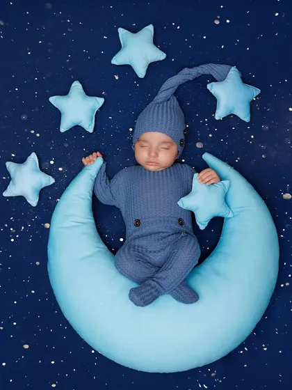 Dreaming on the moon. This classic newborn pose features a baby sleeping on a soft blue crescent moon prop, surrounded by stars.