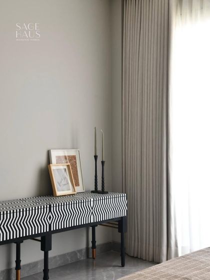 This bedroom corner proves that minimal does not mean boring. A bold, black-and-white bone inlay console adds graphic drama, while the sculptural candle holders and soft curtains keep the space feeling restful and refined.