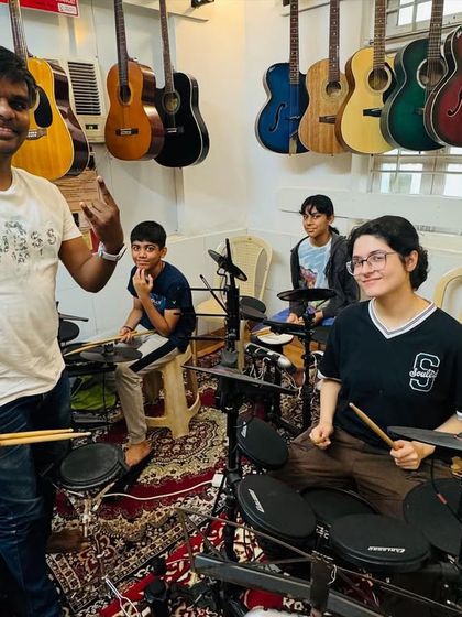 A drum coach with his students in our well-equipped studio. The walls are lined with guitars, creating an atmosphere that is immersive and inspiring for all musicians.