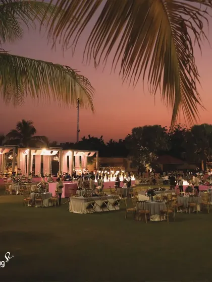 An overview of an outdoor reception at dusk. The warm lighting, elegant seating, and lush green lawn create a magical and romantic atmosphere for an evening of celebration.