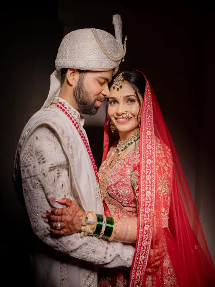 A perfect portrait of the happy couple. My goal is to ensure both the bride and groom look and feel their absolute best, creating timeless memories like this one. This look features classic red lehenga styling with coordinated groom makeup.