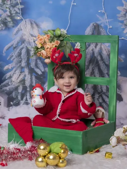 A cheerful Christmas portrait featuring a baby with reindeer antlers. The snowy scene and festive props create a complete and joyful holiday picture.