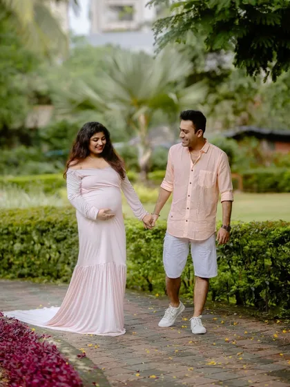 A lovely portrait of an expecting couple walking through a green park. The soft colors of their outfits complement the natural surroundings.