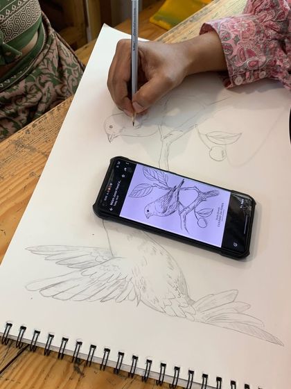 A student practices sketching a bird from a reference photo, focusing on capturing the correct proportions and outline.
