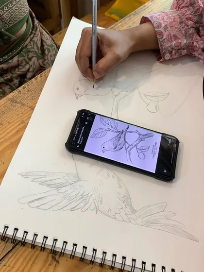 A student practices sketching a bird from a reference photo, focusing on capturing the correct proportions and outline.