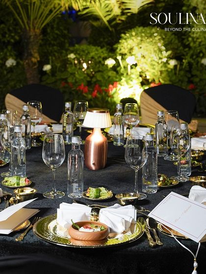 An elegant outdoor table setting for a sit-down dinner, featuring black velvet tablecloths and gold-plated tableware. Every detail is curated to create an immersive and luxurious experience.