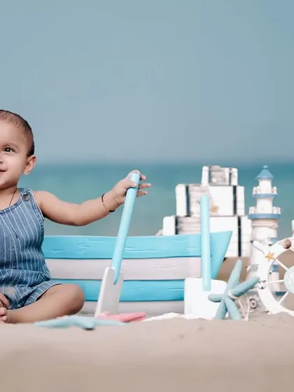 A happy little boy playing on the sand with his nautical toys. The beautiful blue ocean in the background completes this perfect beach day scene.