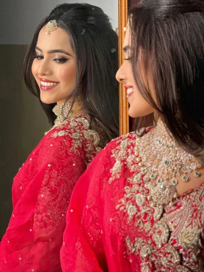 A happy bride in a bright pink lehenga, her smile captured in the reflection of a mirror. The makeup is glamorous and joyful.