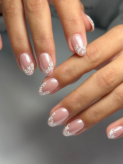 For the bride who loves timeless elegance, these nails feature delicate, lace-like white floral patterns painted over a sheer nude base. It's a classic and sophisticated choice.