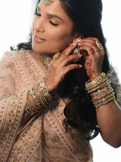 A candid moment of the bride putting on her earrings. The soft lighting highlights the glowing skin and the delicate shimmer on her eyes.