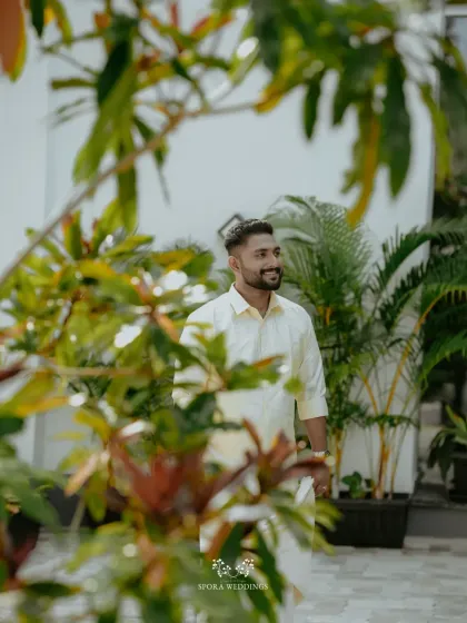 A candid shot of the groom, framed by lush green foliage, capturing a moment of quiet anticipation.