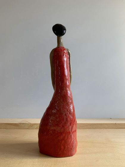 A back view of the "Damn Red Woman" sculpture. Even from behind, the posture and form convey a story of carrying burdens with grace.