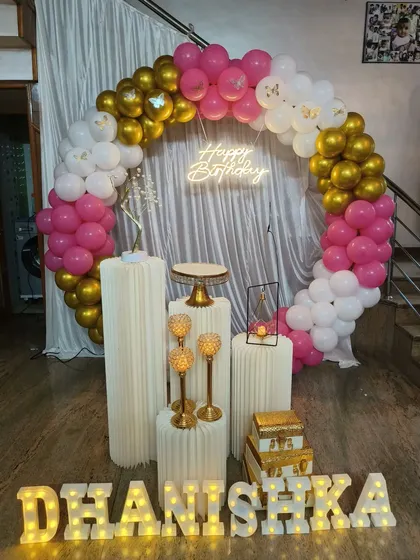A chic pink, white, and gold balloon ring for Dhanishka's birthday. This elegant setup includes butterfly accents, gold candle holders, and an illuminated name sign.