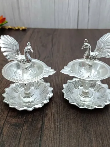 A pair of two-tiered German silver diyas, each with a peacock on top, a classic and much-loved design.