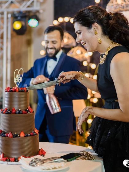 Another angle of this happy couple enjoying their wedding cake moment. The rich, multi-tiered chocolate and berry cake stands as a beautiful centerpiece for their celebration.