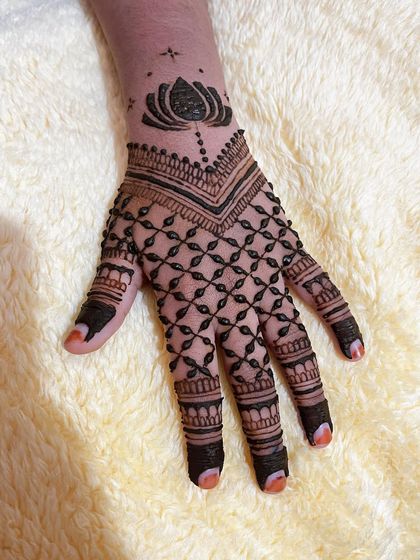 A full hand design with a V-shaped wrist cuff and a dense grid pattern on the palm and fingers. A single lotus motif sits at the top.