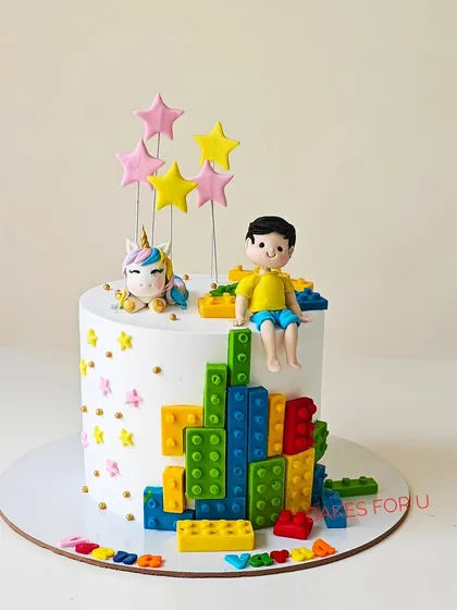 A special cake designed for twins, featuring a boy and a unicorn sitting atop a tower of colorful Lego blocks. This design cleverly combines two different themes into one cohesive and celebratory cake.