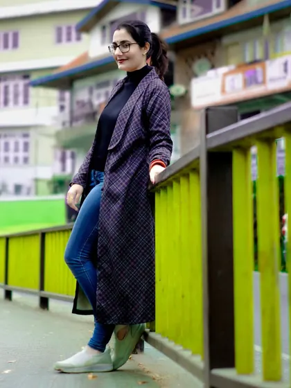 A casual and chic portrait of a woman in a long coat. The urban setting with the bright green railing provides a nice contrast and framing.