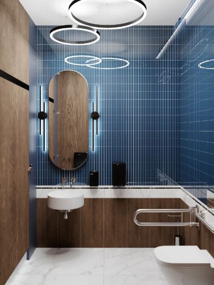 A bold bathroom design featuring deep blue vertical tiles and circular ceiling lights. The wood accents and accessible grab bar near the toilet show our commitment to both style and practical safety.