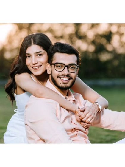 A warm and joyful portrait taken during golden hour. The woman embraces her partner from behind, both smiling at the camera, creating a photo that feels both posed and genuinely happy.