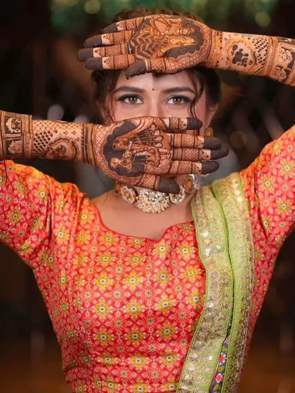 A creative pose showing the bride's eyes between her mehndi-covered hands, which feature a baraat procession scene.