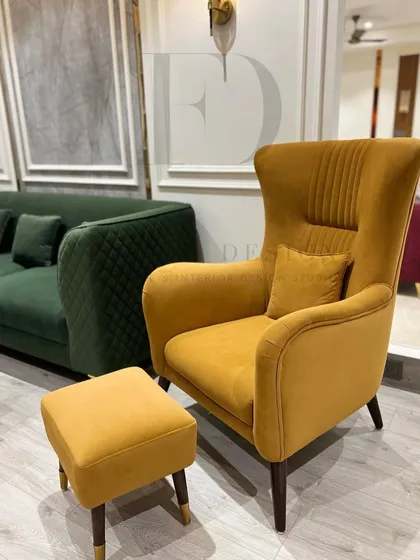 A mustard yellow wingback chair with a matching ottoman. The chair features subtle vertical tufting on its back, adding a touch of texture to its clean, modern lines.