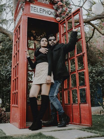 A fun and stylish pose of a couple in a red telephone booth, perfect for a quirky, urban-themed shoot.