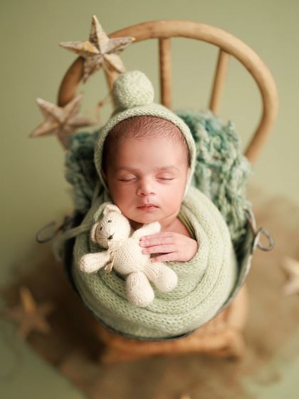 Wrapped in a beautiful sage green color, this little one is just adorable. The pom-pom bonnet and tiny teddy bear add a touch of whimsy to this heartwarming shot.