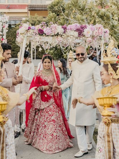 The bride's grand entrance under a floral canopy held by her father, with traditional Thai performers leading the way.