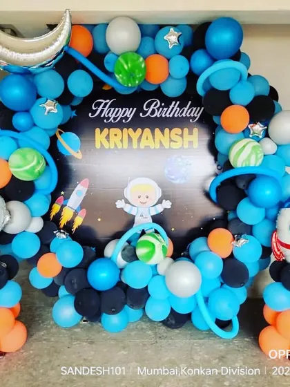 A space-themed balloon arch for a home birthday party. The decoration includes an astronaut foil balloon, a rocket, and planet-like balloon arrangements.