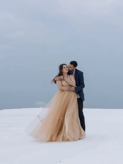 A breathtaking portrait in a surreal, snow-like landscape. The bride's flowing golden gown provides a stunning contrast against the white ground, creating a truly magical and ethereal image.