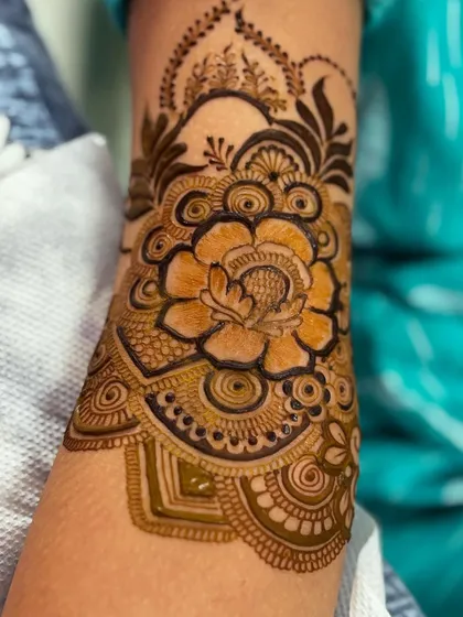 The cuff design on the upper arm, featuring a large, beautifully detailed flower. This is a great way to finish off a full-sleeve mehendi.