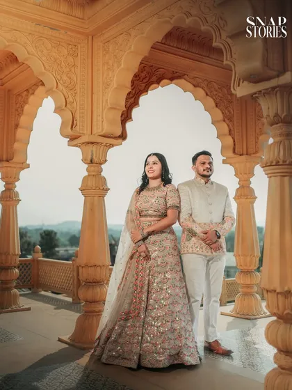 A regal portrait of the couple in traditional attire, standing in a beautifully carved archway overlooking the landscape. A classic pose for a heritage pre-wedding shoot.