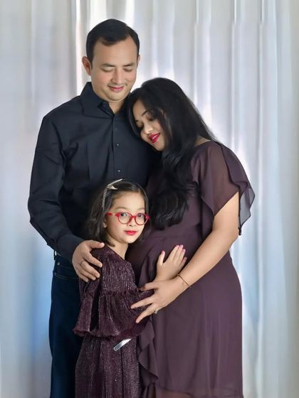 A beautiful maternity portrait of a growing family. The parents and their daughter lovingly embrace the mother's baby bump, capturing their excitement for the new member.