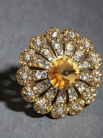 A stunning adjustable finger ring with a large yellow stone surrounded by smaller sparkling stones.