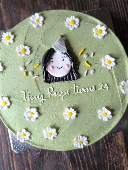 This larger cake showcases a cute and simple bento-style design. It features a hand-drawn portrait for the birthday girl, surrounded by a field of sweet, simple daisies.