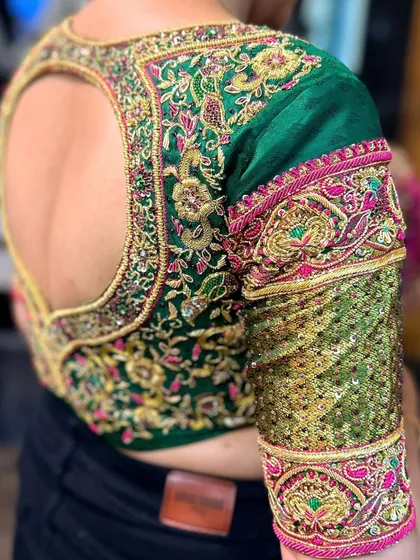 A close-up of the sleeve of the green open-back blouse, showing a combination of zardosi work and a panel of gold sequins.
