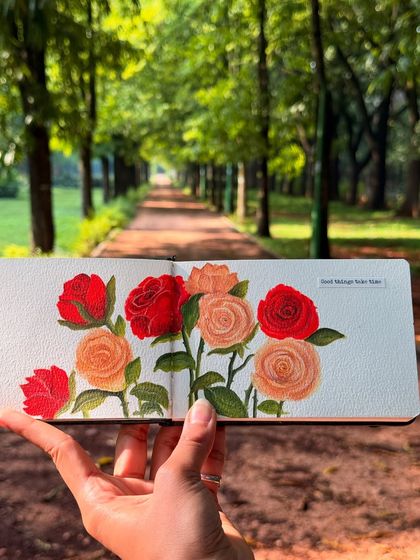 Taking my art outdoors connects it back to its source. Here is the finished rose painting from my sketchbook, held up against a beautiful, serene park path. It shows how nature is the ultimate inspiration for my work.