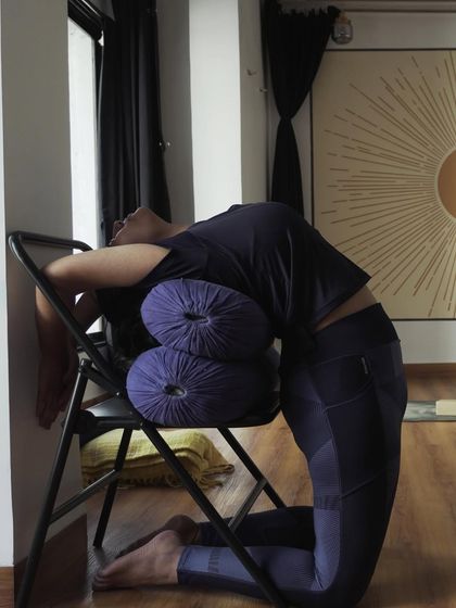 A student uses a chair and bolsters for a supported backbend. This demonstrates our use of props to make yoga accessible and to help students deepen their practice safely.